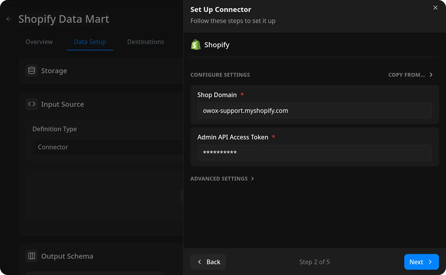 Shopify Data Mart setup connector modal showing configuration fields for connecting to a Shopify store. The modal header reads Set Up Connector and provides step-by-step instructions. The Shopify logo is displayed. Two required fields are shown: Shop Domain with the value owox-support.myshopify.com and Admin API Access Token with masked characters. A Next button is highlighted in blue at the bottom right, and a Back button is at the bottom left. The wider environment is a dark-themed application interface with navigation tabs for Overview, Data Setup, and Destinations. The emotional tone is neutral and instructional.